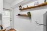 Textured walls featuring two natural wood floating shelves with matte black brackets and an exterior-access door with integrated window blinds