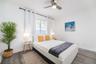 Neutral-toned bedroom featuring wood-finish flooring, a brushed metal ceiling fan with integrated lighting, and a single window framed by an adjustabl