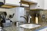 Polished stone countertop and matching full-height backsplash, undermount stainless steel sink, pull-down chrome faucet, and shaker-style cabinetry wi