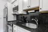 Kitchen featuring white shaker-style cabinetry, stone countertops, stainless steel appliances, and a deep-basin stainless steel sink with a high-arch 