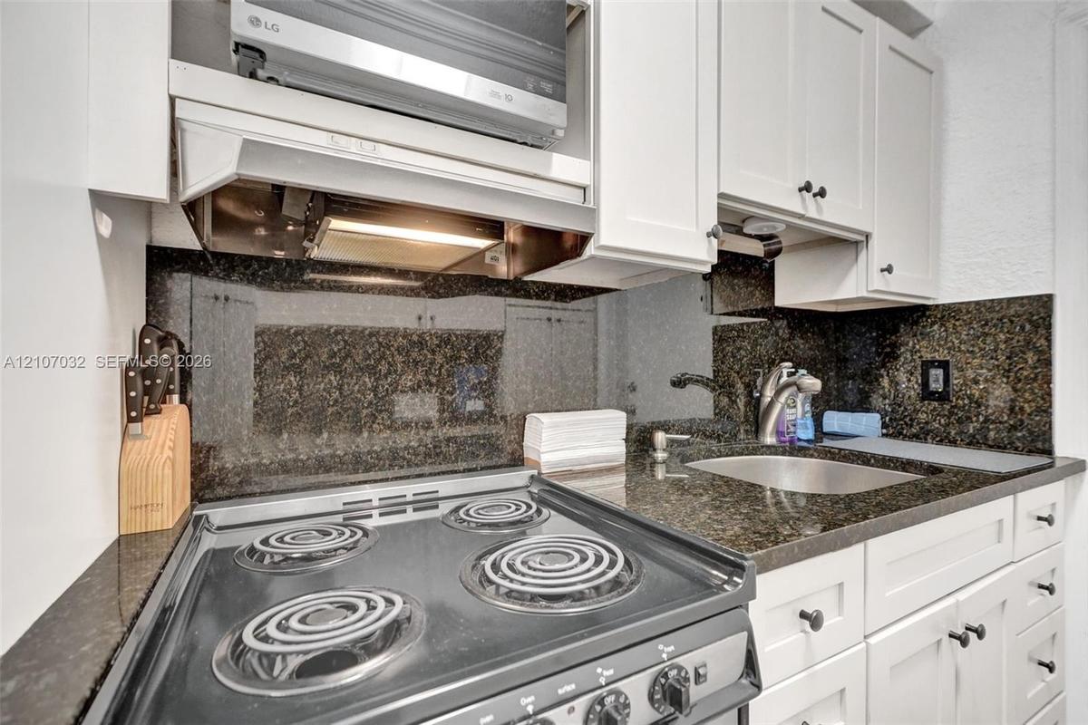 Kitchen featuring white cabinetry, dark stone countertops, integrated backsplash, stainless steel electric range, and an under-mounted sink