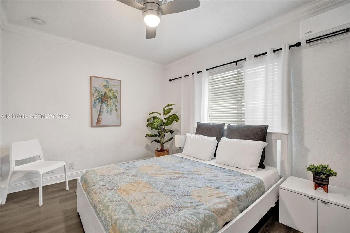 Bedroom featuring wood-finish flooring, crown molding, ceiling fan with integrated lighting, wall-mounted ductless air conditioning unit, and horizont