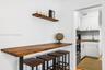 Wall-mounted wooden shelving, custom wood-surfaced breakfast bar, and white shaker-style cabinetry with geometric tile backsplash