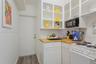 Kitchenette featuring white shaker-style cabinetry, open shelving with glass-front uppers, butcher block countertops, a black undermount sink with a m