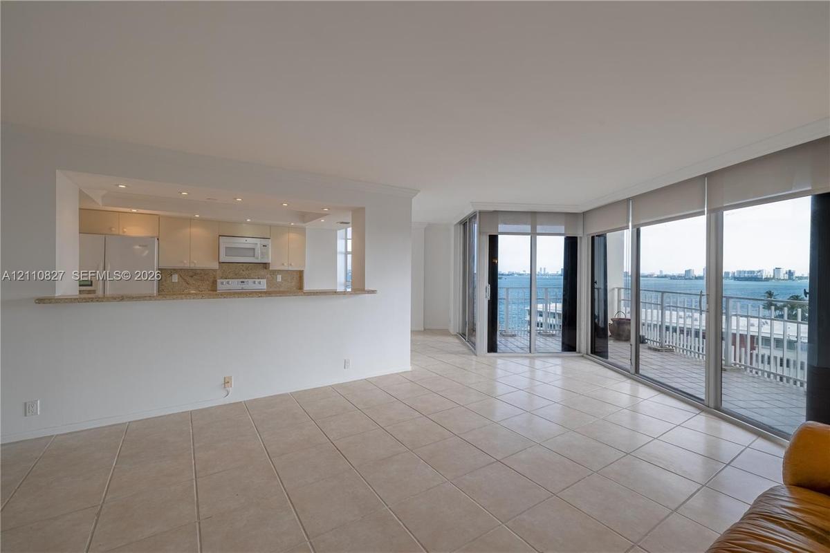Open-concept living space with tile flooring, pass-through kitchen counter, recessed lighting, and expansive floor-to-ceiling glass sliding doors lead