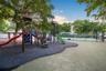 Recreational area featuring a multi-component playground structure, paved sport court, fenced perimeter, and mature canopy trees