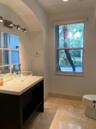 Vanity featuring a dark-toned base, white countertop, and clear glass vessel sink, complemented by a multi-pane mirror, wall-mounted lighting fixture,