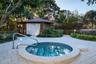 In-ground spa with tile detailing, stone-accented cabana, integrated metallic handrail, and light-toned paver hardscaping