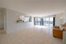 Open-concept area featuring light-toned ceramic tile flooring, a pass-through kitchen counter, and floor-to-ceiling glass sliding doors leading to an 