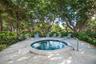 Circular jetted spa with tile interior, stone-paver deck, stainless steel handrail, and mature surrounding landscaping