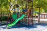 Outdoor recreation area featuring a multi-level playground structure, integrated slide, climbing apparatus, and protective rubberized flooring