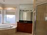 Bathroom featuring a wood-finish vanity with a dark stone countertop, an inset oval soaking tub surrounded by stone tile, a full-height wall mirror, a