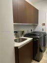 Laundry area featuring flat-panel wood-finish cabinetry, a white countertop, an undermount stainless steel sink, and a high-arc matte black faucet