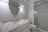 Stone-surfaced vanity with an integrated oval sink, oval wall-mounted mirror, dual-light fixture, and glass-enclosed shower stall
