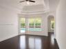 Tray ceiling, wood-finish flooring, and arched entryway featuring large windows and an exterior door providing visibility to the pool area