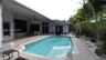 Covered patio with integrated ceiling fan, in-ground pool with stone paver decking, and mature tropical landscaping