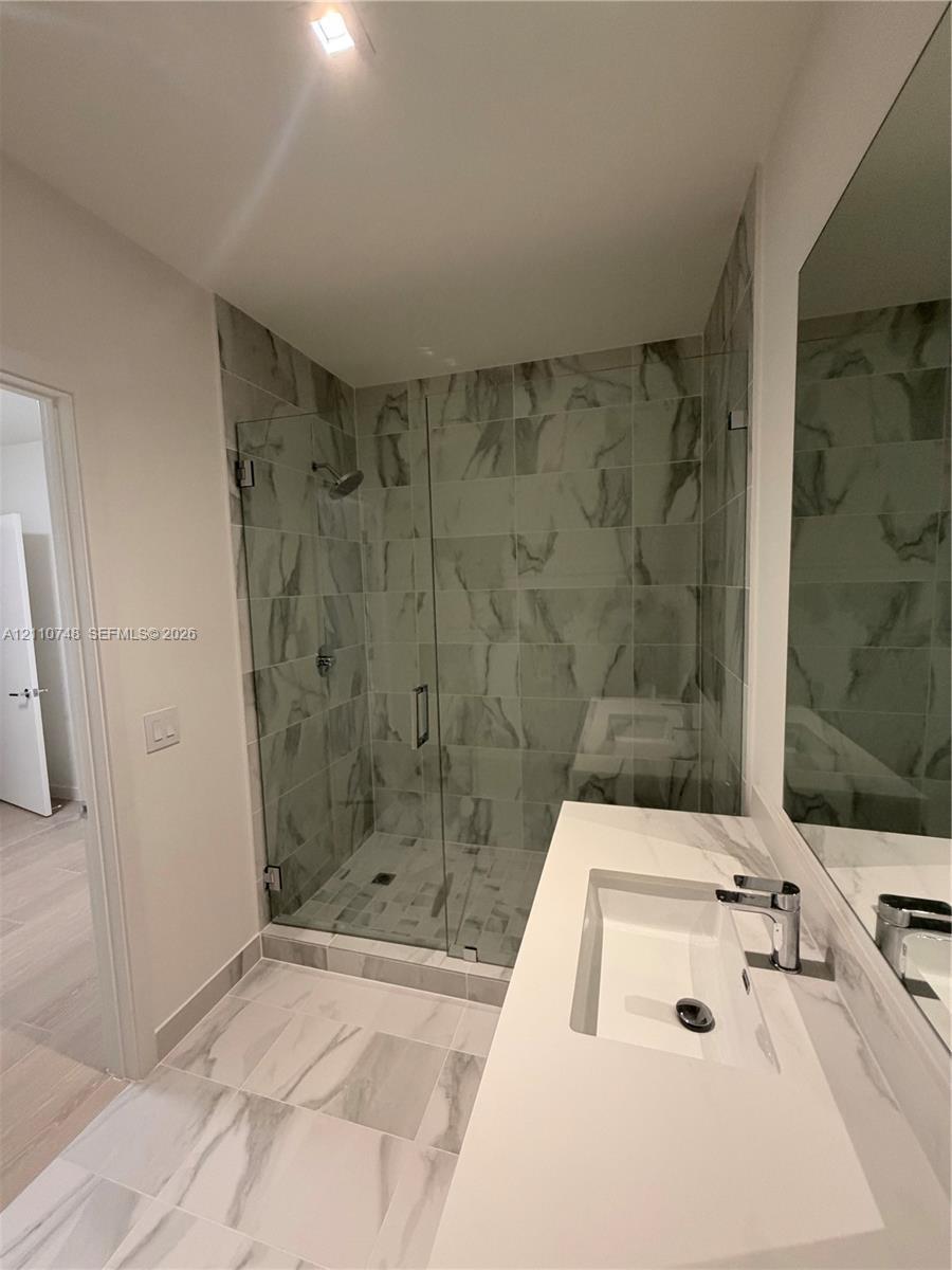 Walk-in shower with floor-to-ceiling tile, frameless glass enclosure, and wall-mounted shower head, paired with a white countertop vanity featuring an
