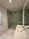 Walk-in shower with floor-to-ceiling tile, frameless glass enclosure, and wall-mounted shower head, paired with a white countertop vanity featuring an
