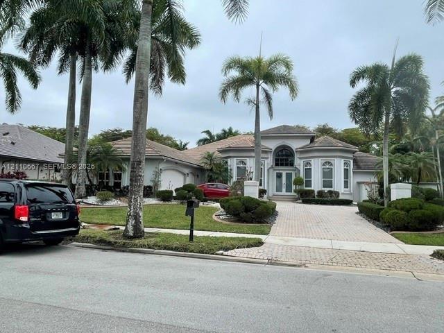 Single-story residence featuring a tile roof, arched entryway with double glass-panel doors, decorative multi-paned windows, and a paved brick drivewa