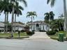 Single-story residence featuring a tiled roof, arched entryway, multi-paned glass double front doors, paved driveway, and mature palm trees