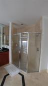 Corner shower enclosure with a metallic frame, neutral stone-finish wall tile, vanity with dark stone countertop, integrated mirror, and patterned til