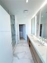 Dual-sink vanity with stone-finish countertop, full-height tile backsplash, glass-enclosed shower, and large-format porcelain tile flooring