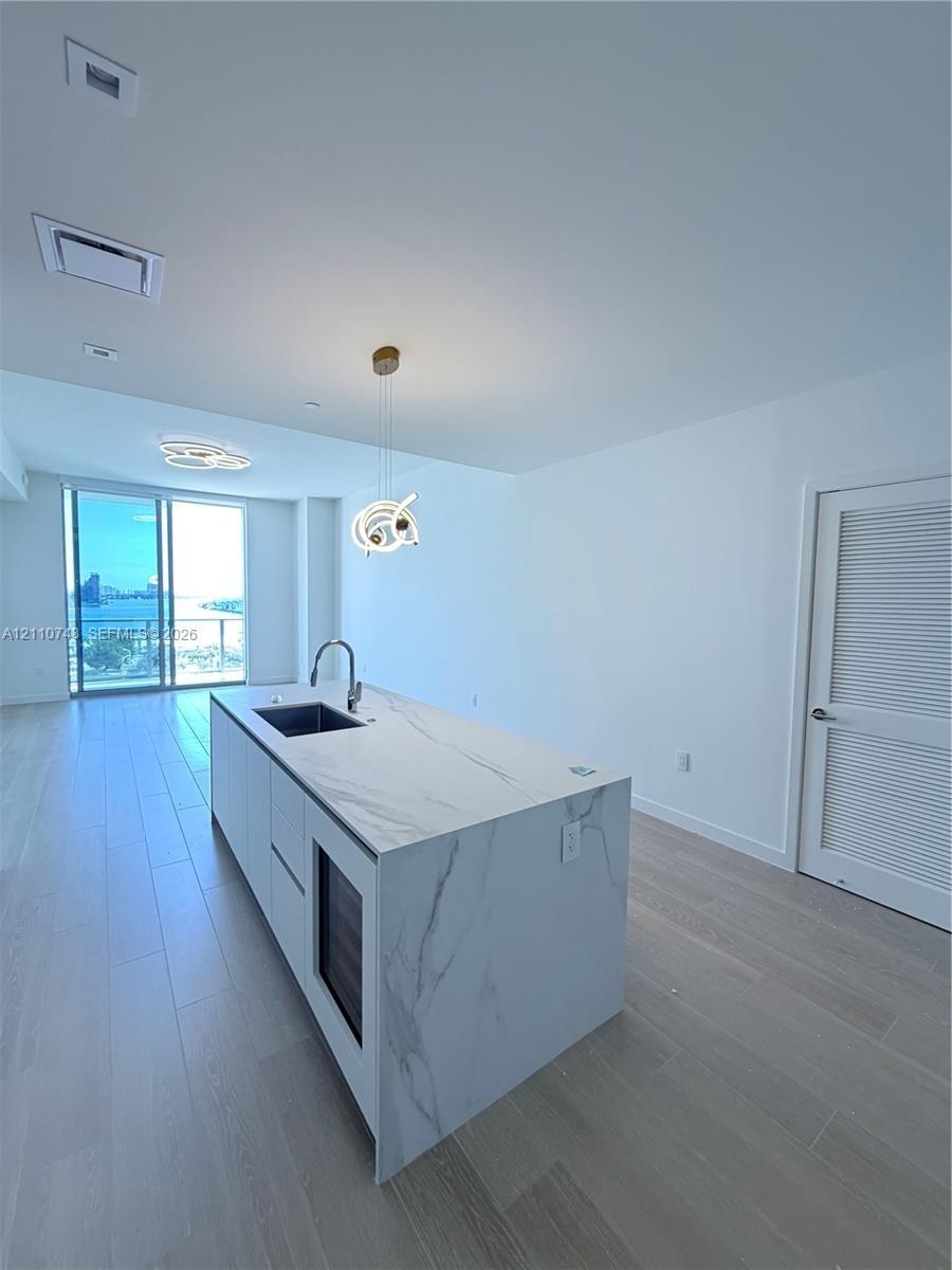 Kitchen island with stone-finish waterfall countertop, undermount sink, built-in wine cooler, and high-arc faucet, complemented by wood-finish floorin