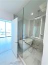 Freestanding soaking tub enclosed in a glass-partitioned wet room featuring floor-to-ceiling stone-look tiling, a ceiling-mounted rainfall showerhead,
