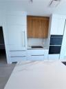 Custom cabinetry featuring contrasting wood-finish uppers and matte white base units, integrated refrigerator, built-in dual oven, stone-surface backs