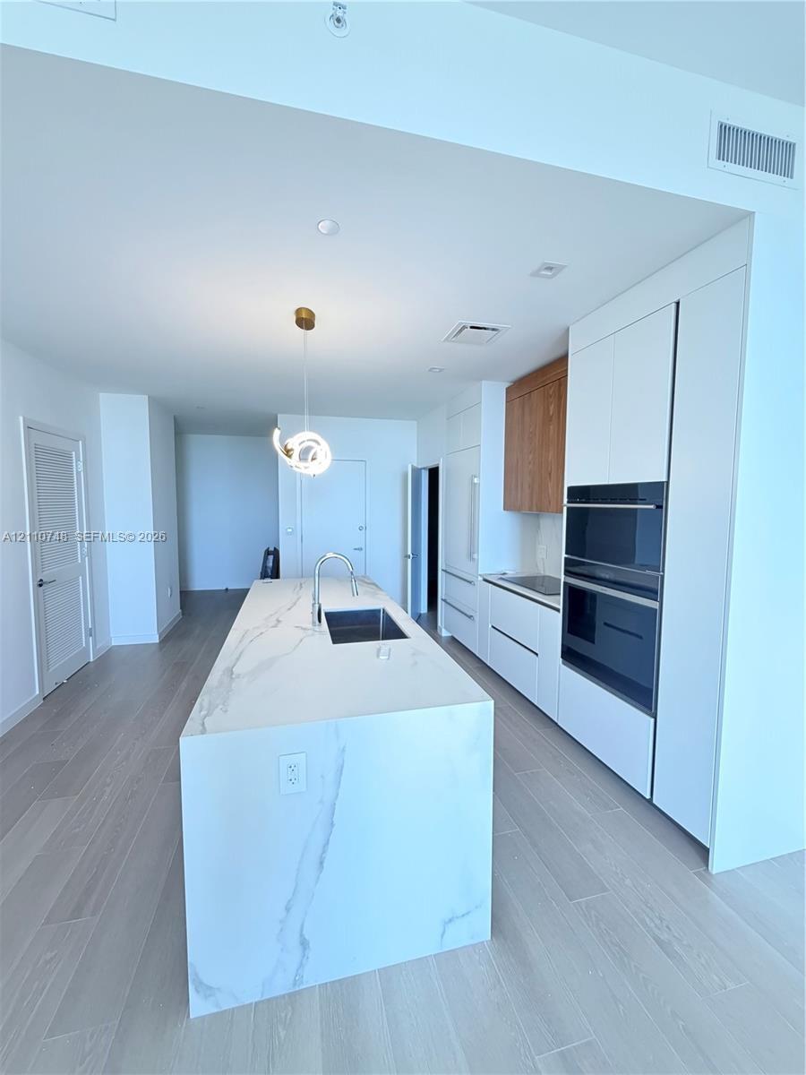 Kitchen featuring a large central island with a waterfall-edge countertop, stone-finish surfacing, integrated sink, and gooseneck faucet, paired with 