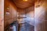 Sauna interior featuring natural wood-paneled walls, built-in tiered wooden benches, slatted wood flooring, and a metal sauna heater with a protective