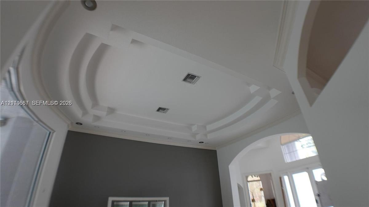 Custom tray ceiling with tiered architectural detailing, integrated recessed lighting, and arched passage entryways