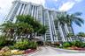 High-rise residential exterior featuring stepped architectural balconies, white concrete facade, covered porte-cochere entry, and extensive tropical l