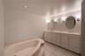 Dual-sink vanity with stone-surfaced countertop, drop-in soaking tub, tile flooring, and wall-mounted round mirrors
