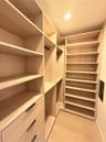 Custom walk-in storage featuring light wood-finish shelving, integrated hanging rods, multi-tier cabinetry, and minimalist matte black hardware
