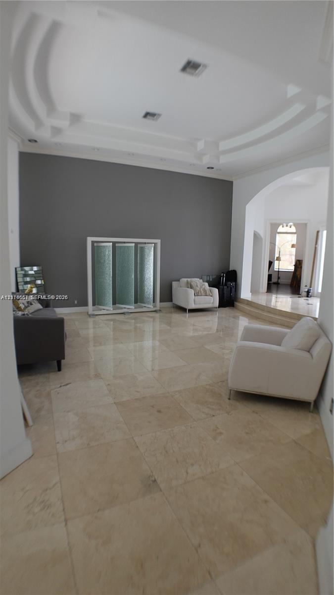 Interior space featuring polished stone flooring, recessed tray ceiling with architectural molding, and an arched entry