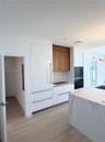Kitchen featuring a stone-surface island, built-in integrated refrigerator, wall-mounted double oven, custom flat-panel cabinetry with wood-finish upp