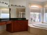 Bathroom featuring wood cabinetry, dark stone-finish countertop with an integrated sink, built-in soaking tub with stone-tile surround, and a large wa