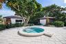 In-ground spa featuring a circular concrete surround, stone-accented exterior structures, and light-toned paver hardscaping
