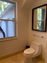 Restroom featuring stone-finish flooring, a wall-mounted rectangular mirror with a dark frame, a glass shelf, and a high-profile one-piece toilet