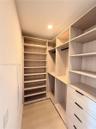 Custom walk-in closet featuring light wood-finish shelving, integrated hanging rods, and a four-drawer built-in storage unit with matte black hardware
