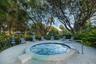In-ground circular spa featuring a stone paver deck, stainless steel handrail, and mature tropical landscaping