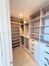 Custom walk-in closet featuring light-toned wood-finish cabinetry, floor-to-ceiling shelving, recessed lighting, and integrated drawers with matte bla
