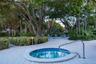 In-ground spa with mosaic tile interior and integrated metal handrail, situated on a stone-paver deck surrounded by mature landscaping