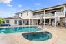 Stucco exterior featuring a dual-level covered patio, stone-finish pool deck, in-ground swimming pool with attached spa, and a white spiral staircase