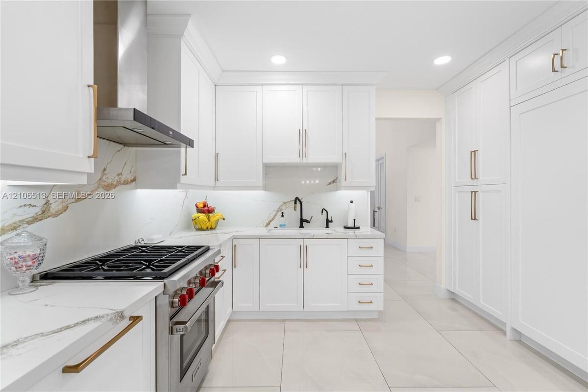 Kitchen featuring shaker-style white cabinetry, stone-finish countertops with matching full-height backsplash, stainless steel gas range with overhead
