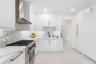 Kitchen featuring shaker-style white cabinetry, stone-finish countertops with matching full-height backsplash, stainless steel gas range with overhead