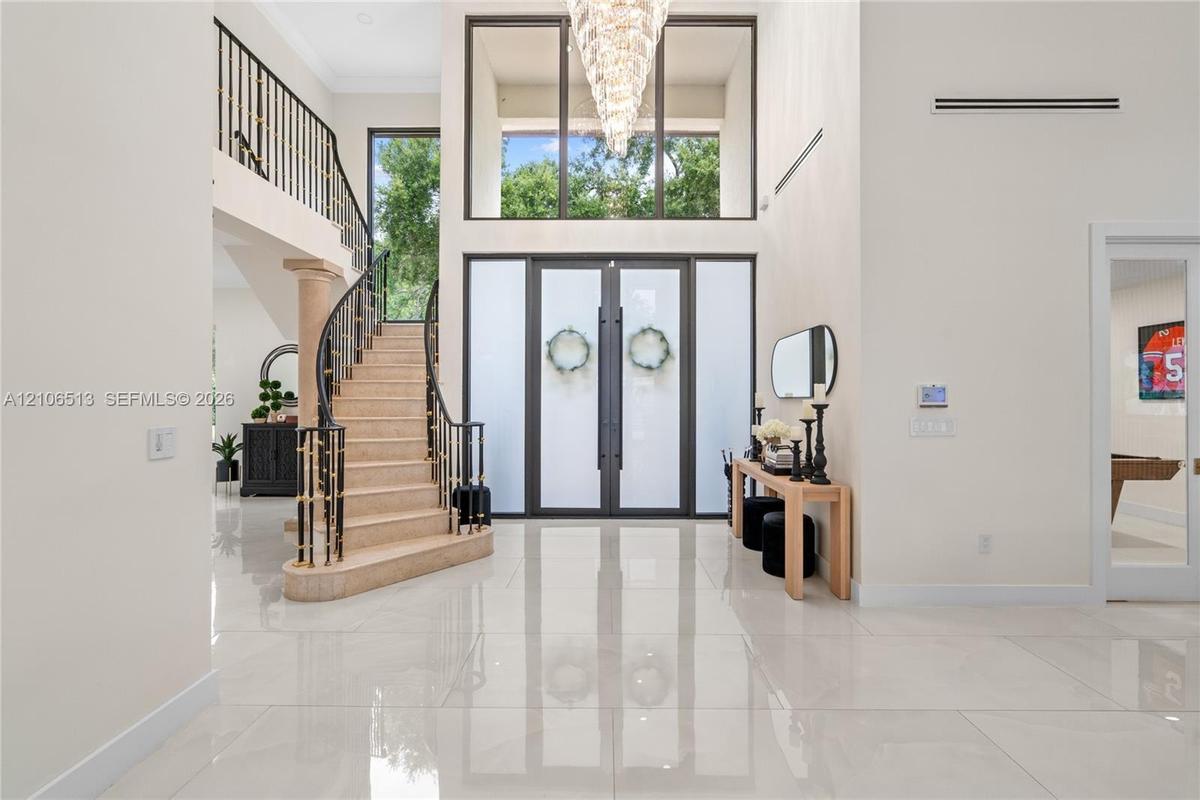 Grand foyer featuring polished large-format tile flooring, double entry doors with frosted glass panels, an expansive multi-story window, a tiered cry