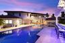 Rear exterior featuring a custom swimming pool with integrated spa, stone-paver decking, built-in swim-up bar, and second-level balcony with white rai