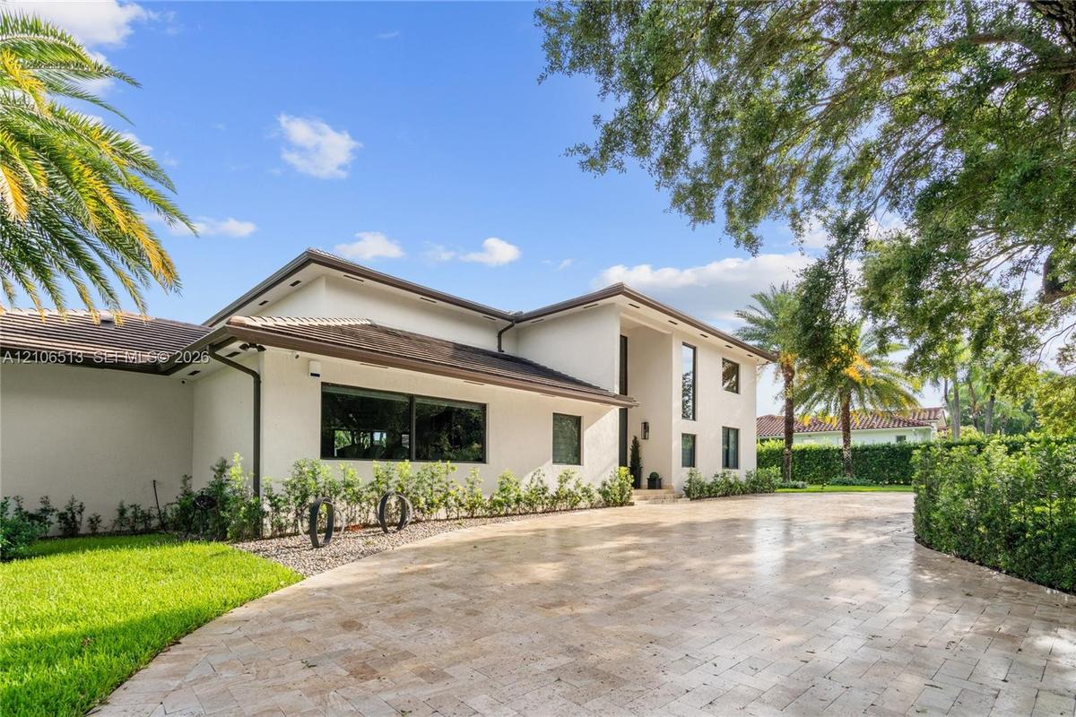 Stucco exterior featuring a low-pitch roof, expansive stone-paver driveway, and mature landscaping